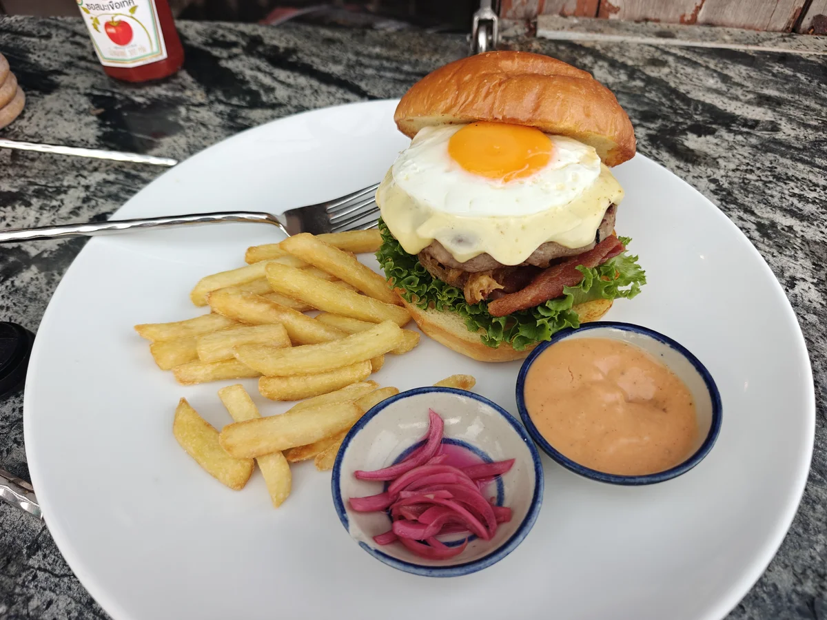 Brioche burger with fried egg, melted cheese, and bacon, served with fries, pickled red onion, and a house sauce on Koh Chang.
